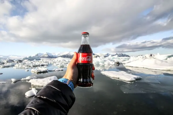 A hand holding up a bottle of Coca-Cola in front of floating icebergs.