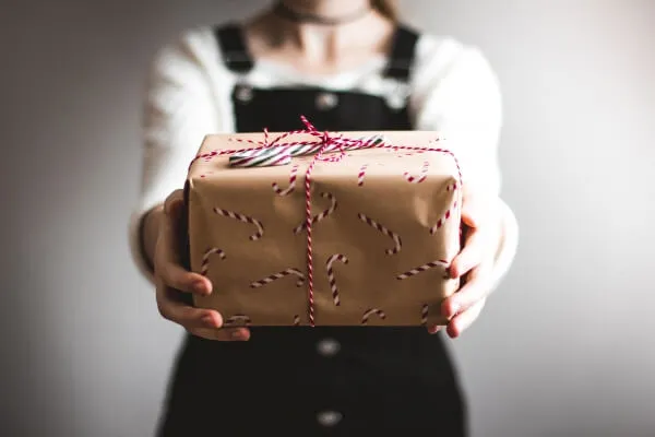 A person holding out a gift wrapped in brown paper and string.