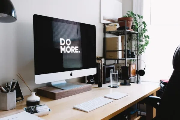 A desk with a computer screen that reads “Do more.”, a keyboard and shelves of plants.